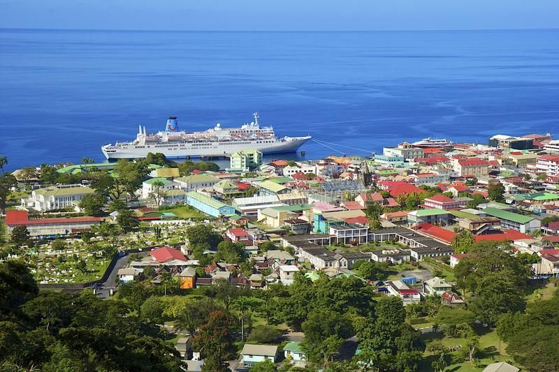 Aerial view of a coastal town with buildings, a cruise ship in the harbor, and the blue ocean in the background.