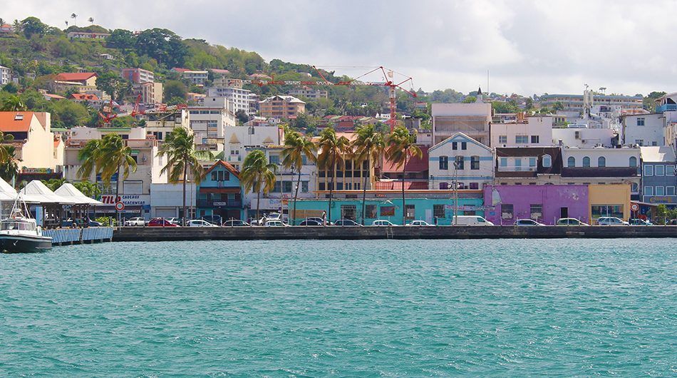 Waterfront view of Fort-de-France, Martinique, with colorful buildings and palm trees against a hillside.