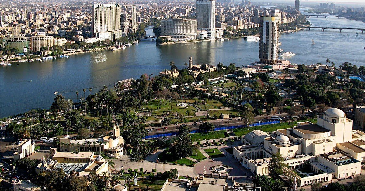 Aerial view of Cairo, Egypt, with the Nile River dividing the city.  Palm-lined island in the foreground with buildings, bridges, and skyscrapers.