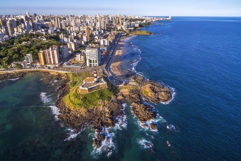 Coastal cityscape of Salvador, Brazil, with a historic fort on a rocky outcrop, buildings, and a beach along the blue ocean.