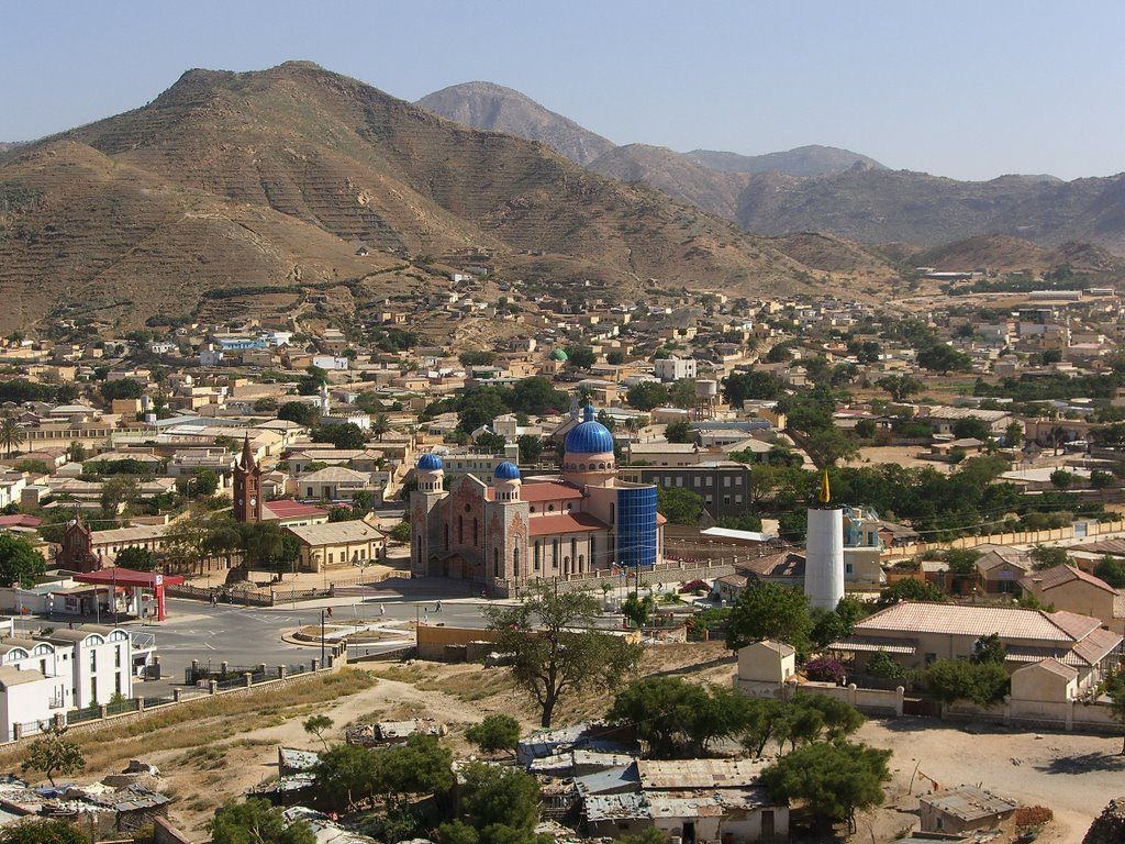 Townscape in mountainous terrain, dominated by a large church with blue domes and a brick facade.