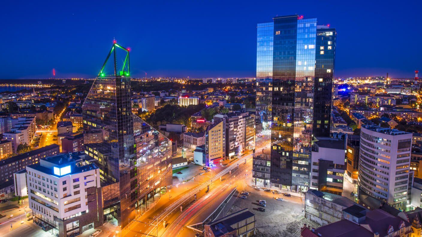 Aerial view of Tallinn, Estonia at night, featuring illuminated skyscrapers and city lights against a dark blue sky.