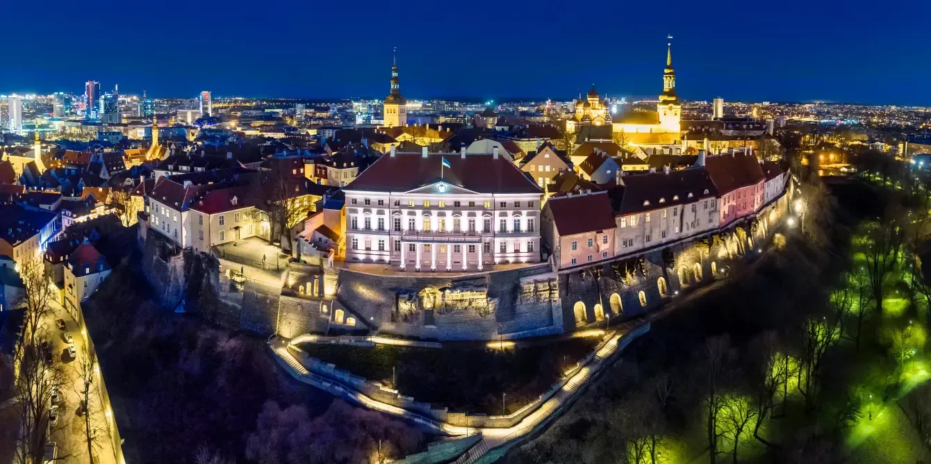 Aerial night view of Tallinn, Estonia, with illuminated buildings and city lights against a dark blue sky.