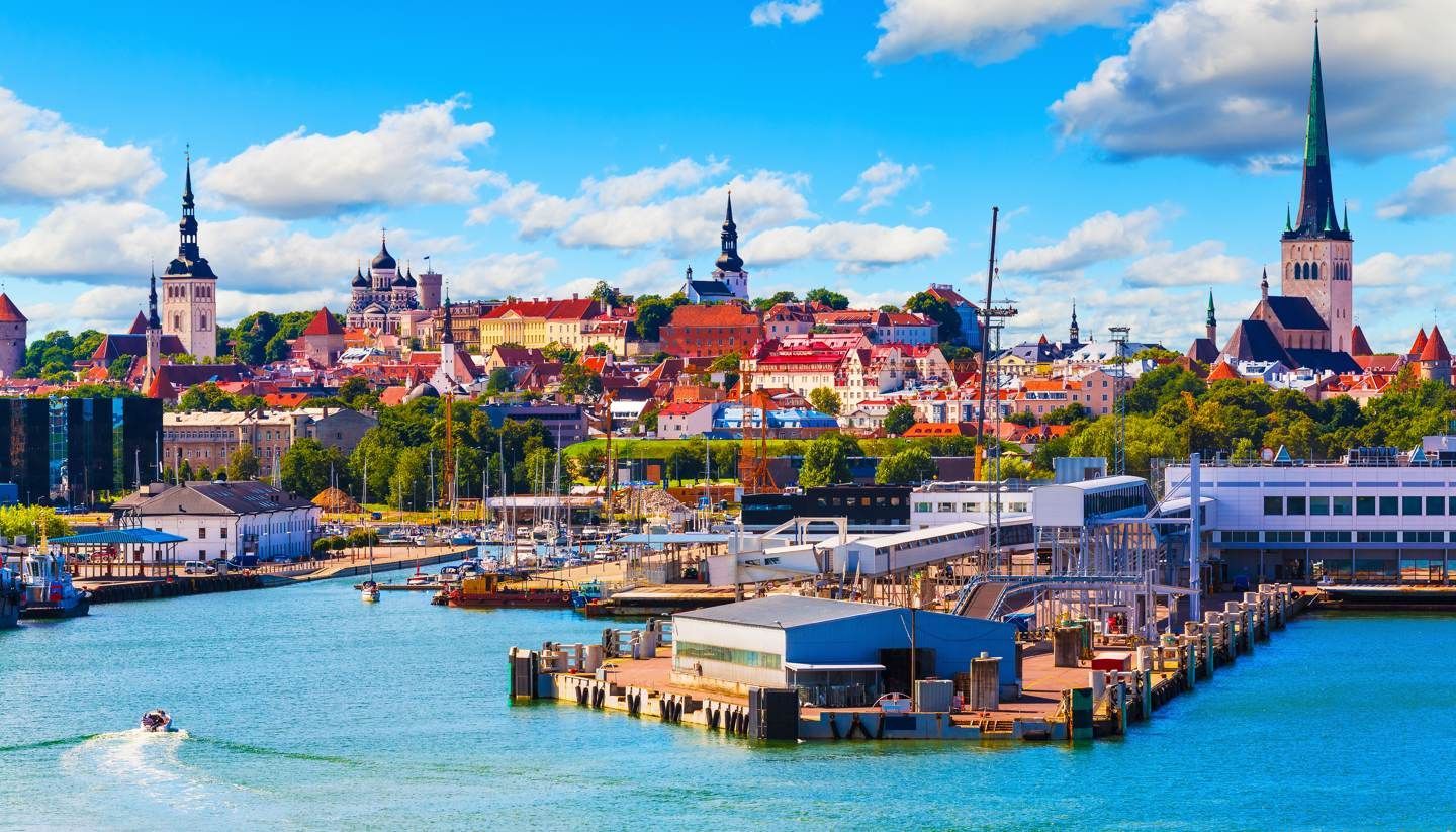 A harbor view of Tallinn, Estonia, with colorful buildings and church spires against a bright blue sky.