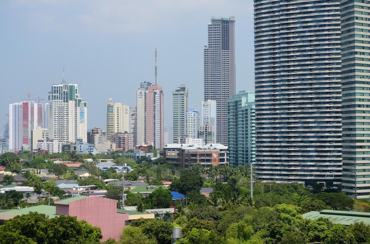 Skyline of modern high-rise buildings with a foreground of trees and lower buildings, under a clear sky.