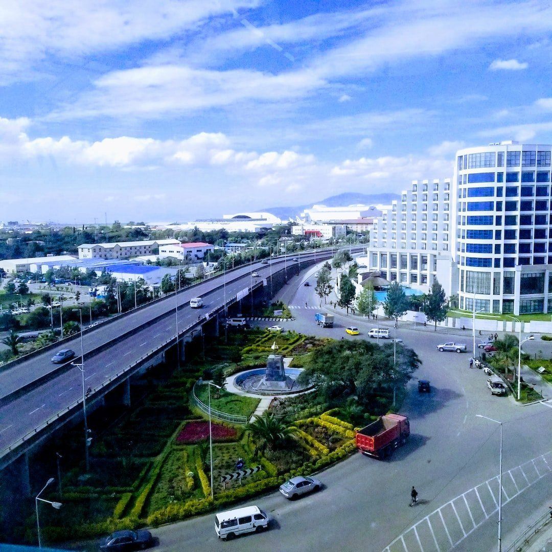 A city view with a highway overpass, fountain, and modern buildings under a blue sky.