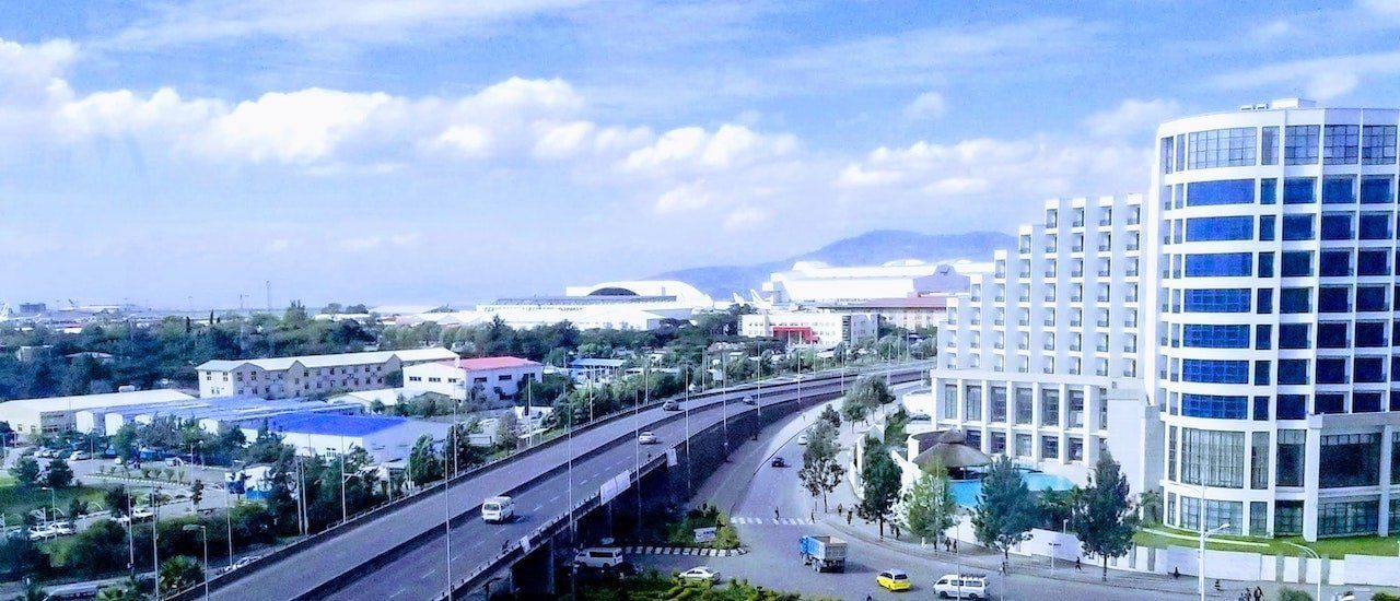 Cityscape with a multi-lane highway, modern buildings, and a partly cloudy sky.