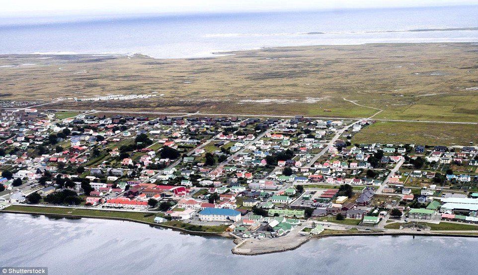 Aerial view of Stanley, Falkland Islands, a town nestled on the coast. Buildings of various colors border the waterfront and extend inland.