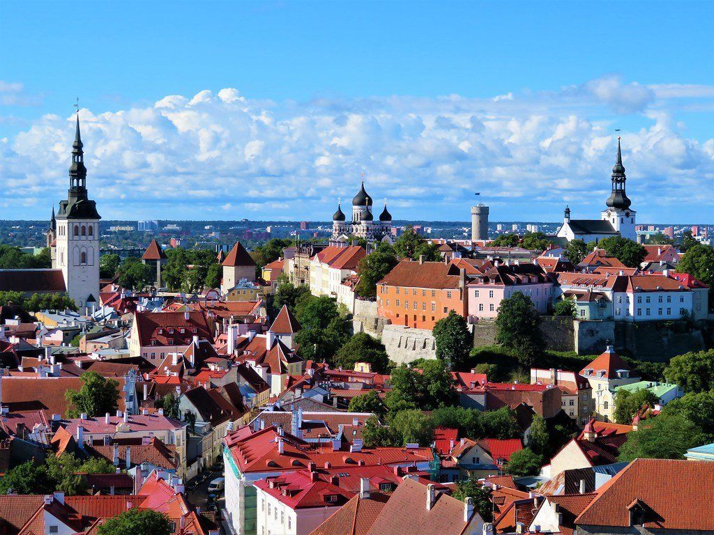 View of Tallinn, Estonia, with red-roofed buildings, church spires, and a blue sky filled with clouds.