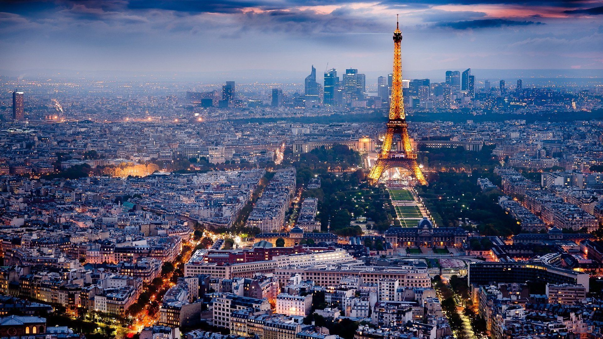 The Eiffel Tower illuminated at night in Paris, France. City lights stretch to the horizon under a twilight sky.