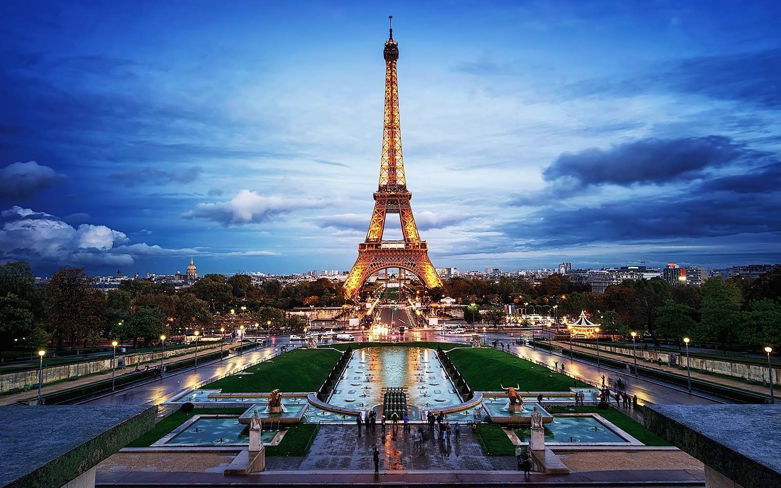 Eiffel Tower lit up at dusk, reflected in the water of a formal garden in Paris, France.