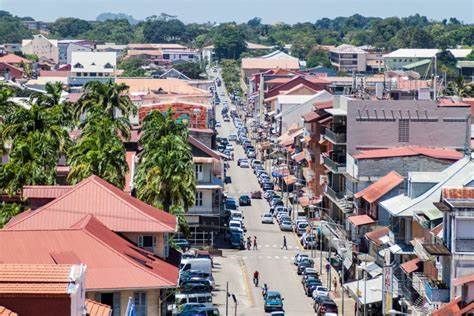Street scene in Cayenne, French Guiana, with rows of buildings, vehicles, and people on the road under a clear sky.
