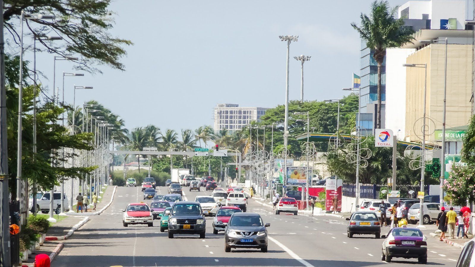 Busy city street with cars and trucks, trees, and buildings under a bright sky.