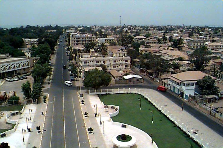 An aerial view of a wide, tree-lined street in a city with multi-story buildings and green spaces.