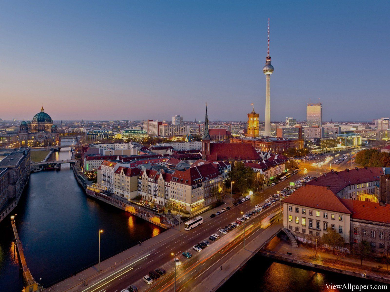 Berlin skyline at dusk, featuring the TV Tower, cathedral, and river Spree. Buildings glow with warm lights.