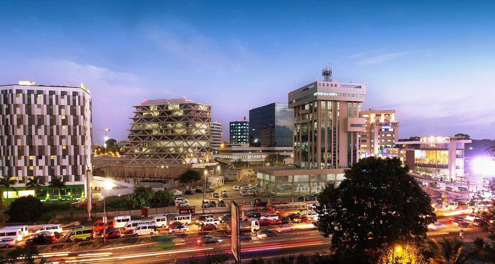 City skyline at dusk in Accra, Ghana, with modern high-rise buildings and traffic.