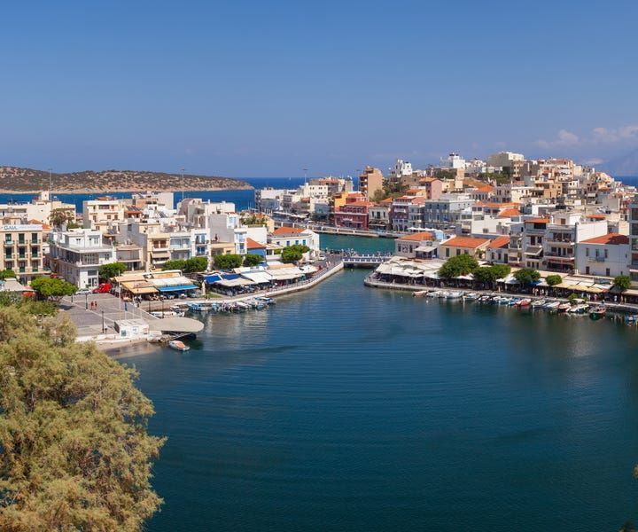 Coastal town with white buildings, restaurants, and boats on a blue lake under a clear sky.