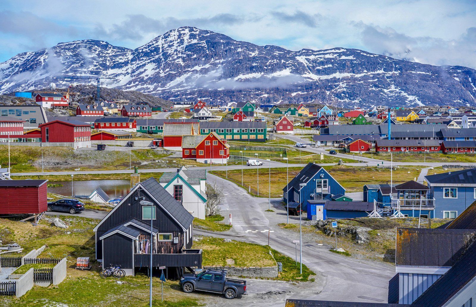 Colorful houses in a town on a coastal landscape, with snow-capped mountains in the background.
