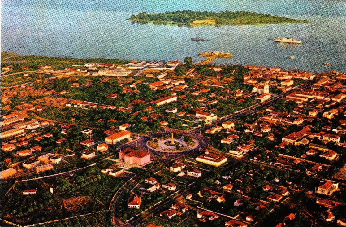 Aerial view of a coastal town with a circular monument at its center, an island in the background, and a body of water.
