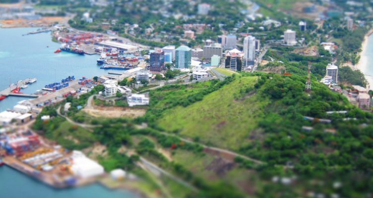 Aerial view of Port Moresby, Papua New Guinea, with harbor, city buildings, and a lush green hill.