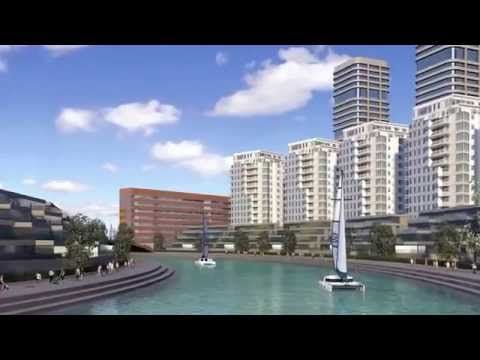 A waterfront cityscape with tall buildings, a canal, and sailboats under a blue sky. People walk along the canal's edge.