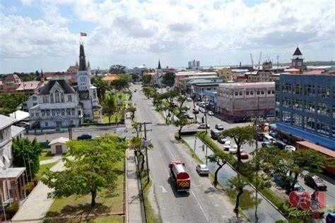 A wide street in Georgetown, Guyana, lined with trees and buildings. A fire truck drives down the road.