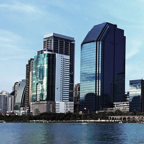City skyline with tall, modern buildings reflecting the blue sky and water in the foreground.