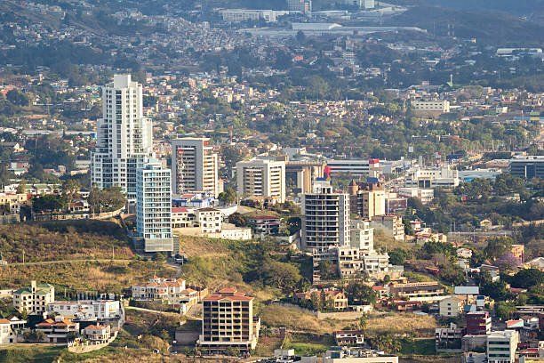 Cityscape with high-rise buildings and residential areas on a hillside under a sunny sky.