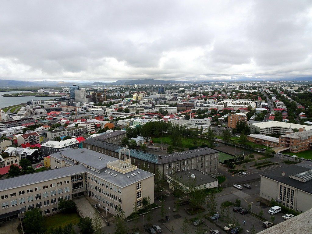 Aerial view of Reykjavik, Iceland, under a cloudy sky. Buildings of various heights and colors spread across the city, with mountains in the distance.