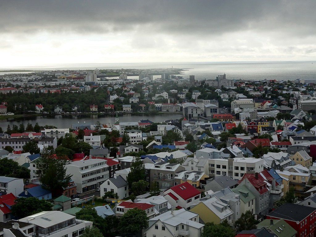 Overhead view of Reykjavik, Iceland, with colorful buildings, a lake, and the sea under a cloudy sky.