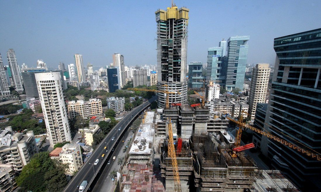 High-angle view of Mumbai cityscape, featuring skyscrapers, ongoing construction, and a highway with traffic under a clear sky.