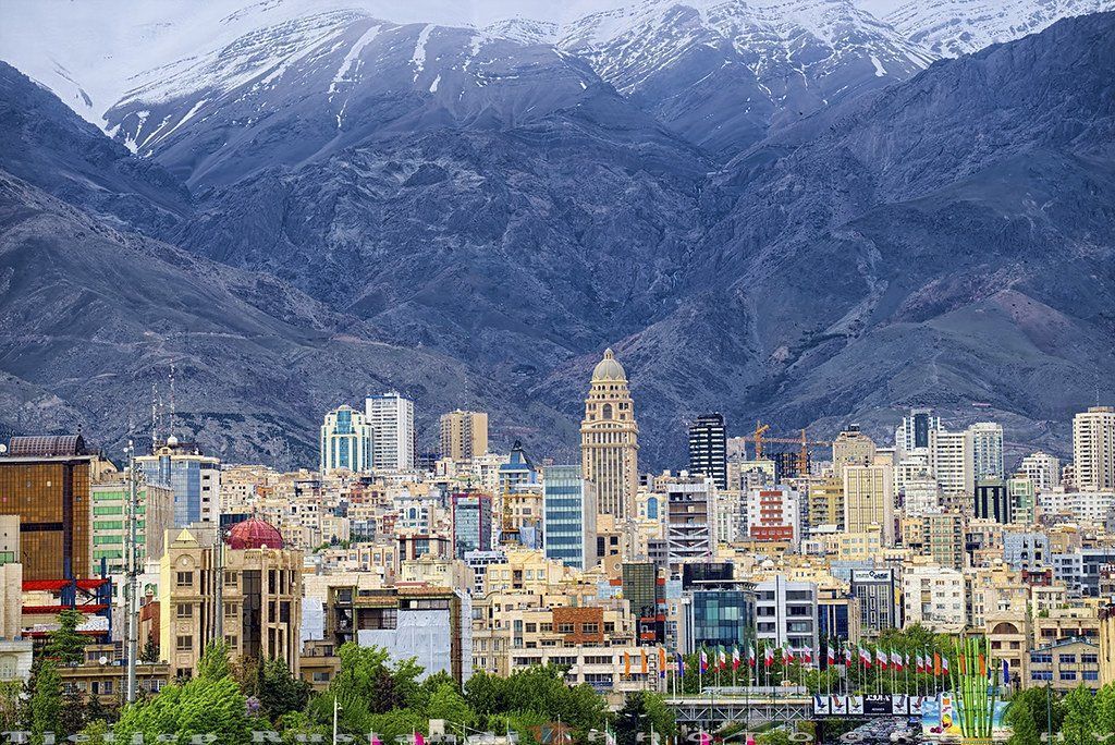 City skyline with buildings of various heights and styles, backed by snow-capped mountains.
