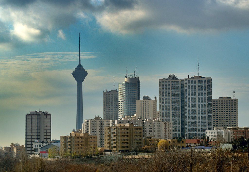 Tehran skyline dominated by Milad Tower, with modern high-rise buildings under a cloudy blue sky.