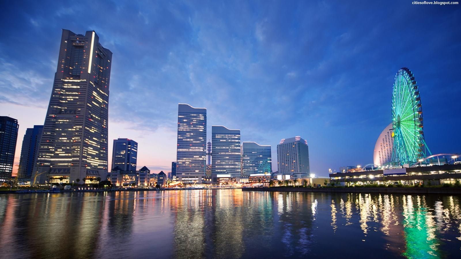 Night skyline of Yokohama, Japan, with illuminated skyscrapers and a Ferris wheel reflected in the water.