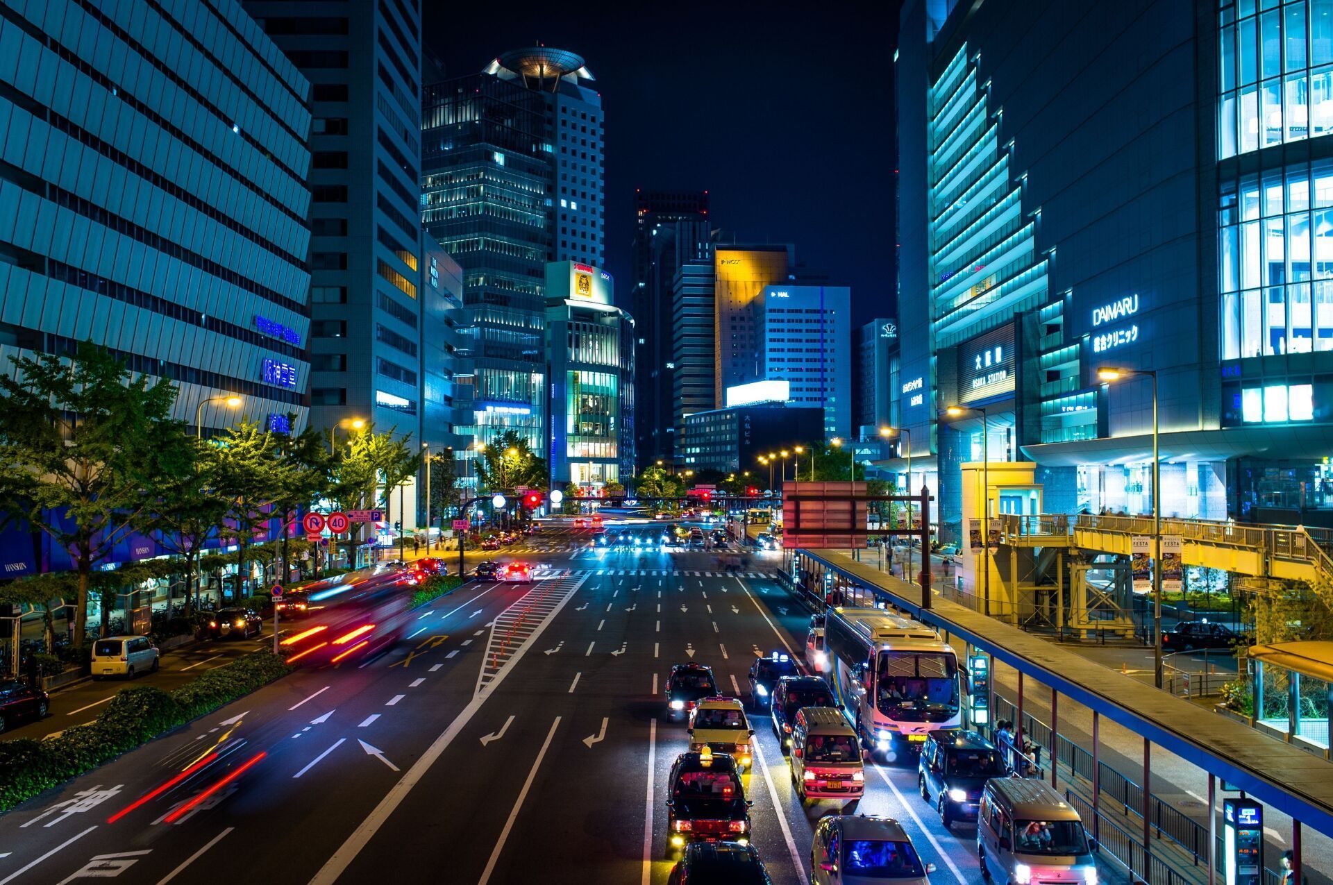 Nighttime city street scene with illuminated skyscrapers, traffic, and streetlights.