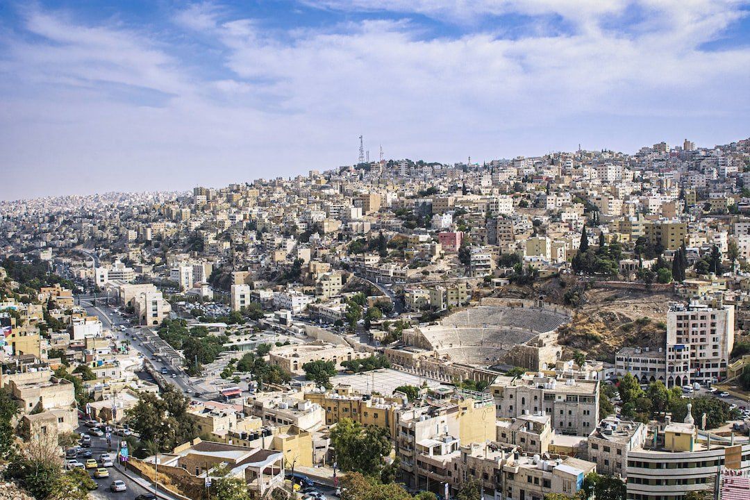 View of Amman, Jordan, a densely packed city on a hillside, including buildings, roads, and a Roman theater.