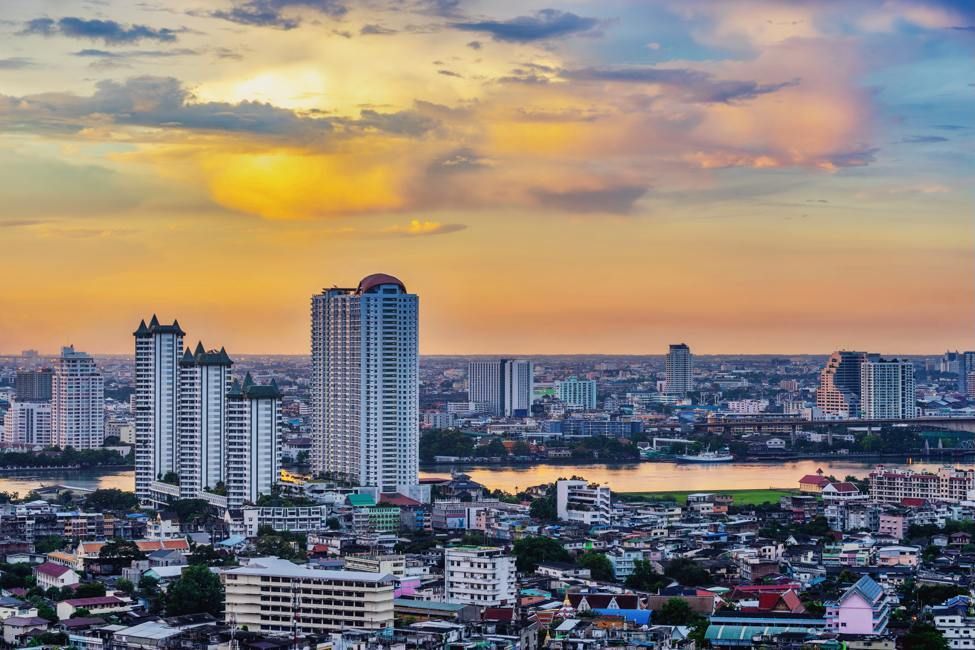 City skyline at sunset, featuring tall buildings, a river, and an orange and yellow sky.