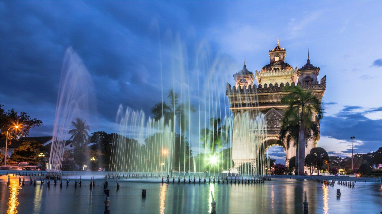 Water fountain in front of Patuxay Monument in Vientiane, Laos, illuminated at dusk.
