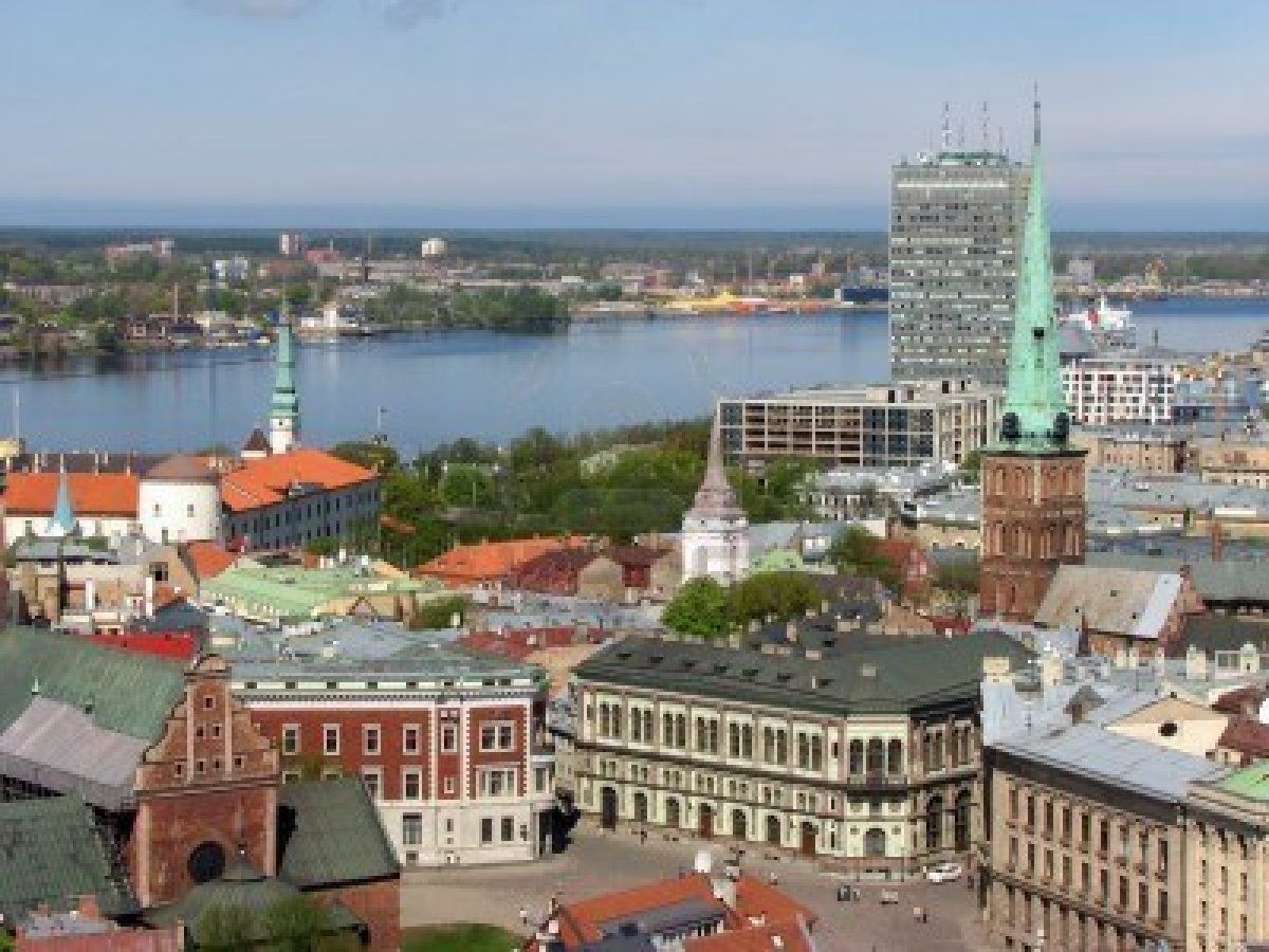 Cityscape of Riga, Latvia, with colorful buildings, church spires, and a tall modern skyscraper along a river.