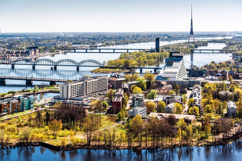 Aerial view of Riga, Latvia, showcasing bridges over the Daugava River, the National Library, and the television tower on a sunny day.