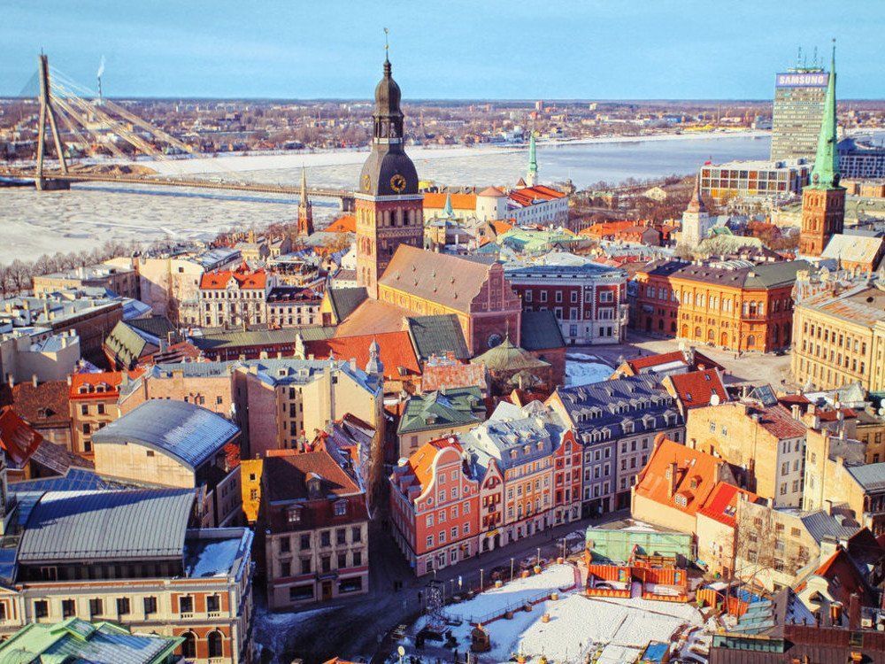 Aerial view of Riga, Latvia, with colorful buildings, a tall church, and a river with a bridge in the winter.