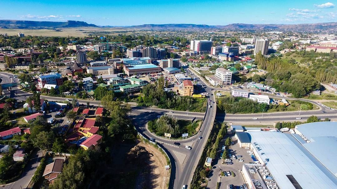 Aerial view of a city with buildings, roads, and green spaces under a bright blue sky.