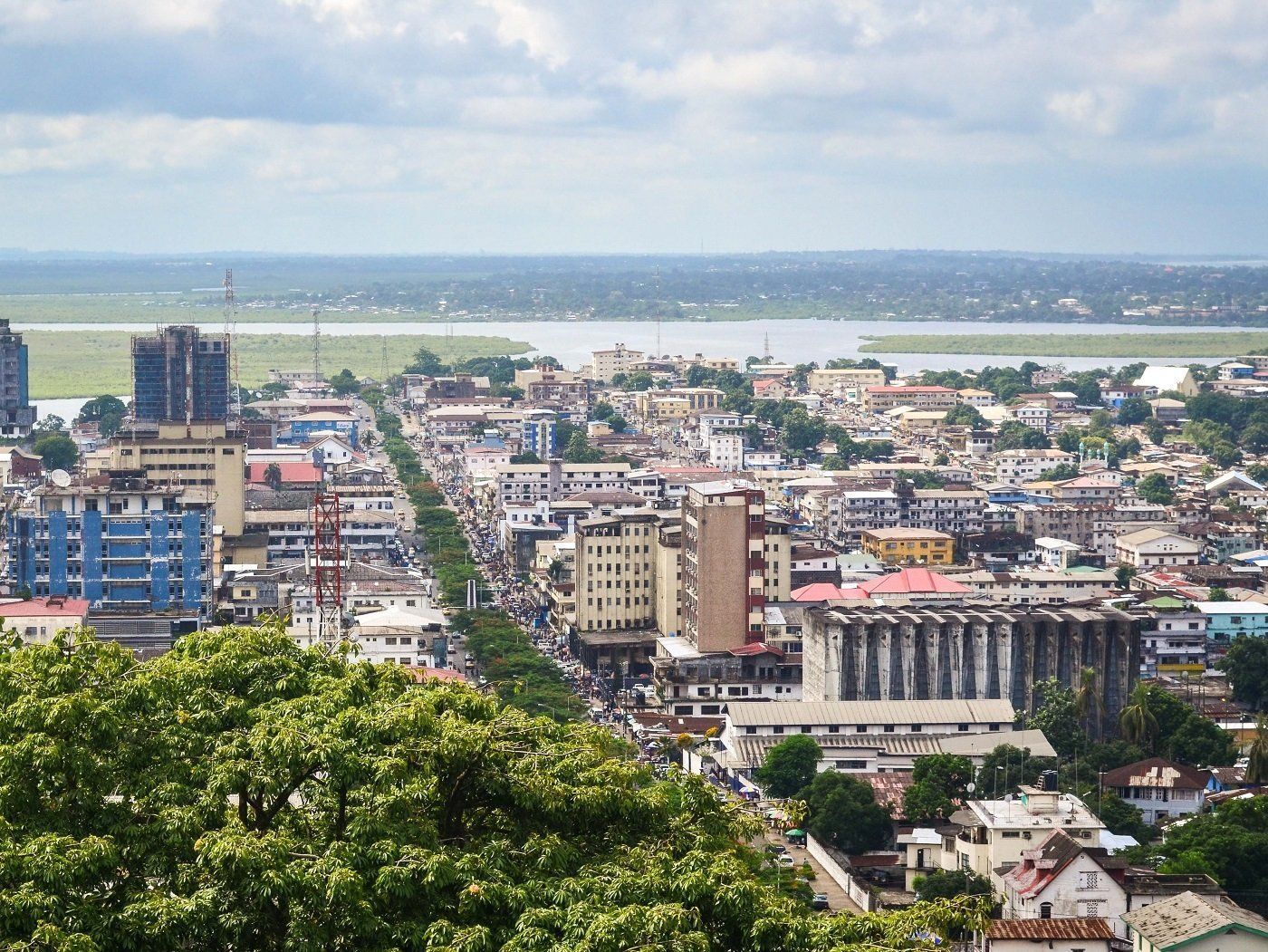 Overhead view of a city in Africa with tall buildings, a wide road, and a body of water in the distance under a cloudy sky.