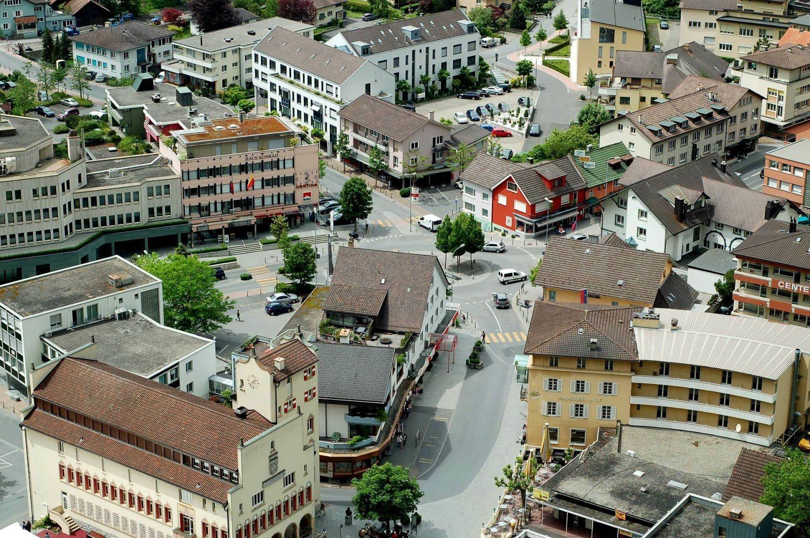 Aerial view of a town square with various buildings and roads, featuring different colored roofs and a mix of architectural styles.