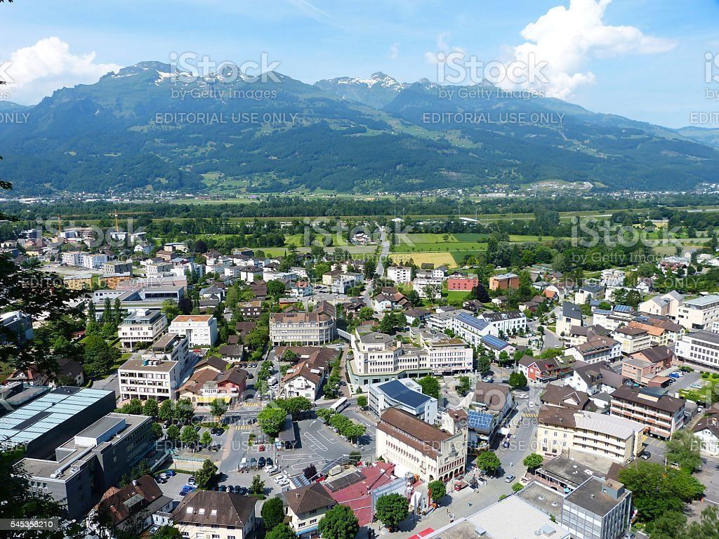 Town nestled in a valley with mountains in the background under a clear, blue sky.