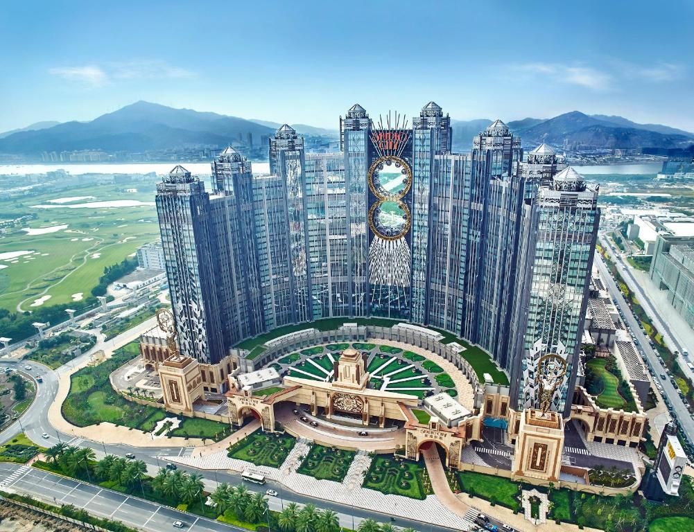 Aerial view of the Grand Lisboa Palace resort in Macau, China. Multiple tall, ornate towers surround a circular garden and central entrance.