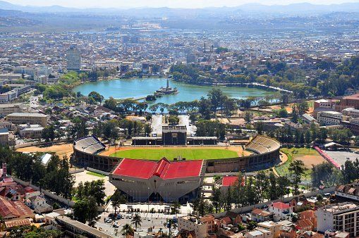 Panoramic view of Antananarivo, Madagascar, with a stadium in the foreground, lake in the center, and city buildings in the background.
