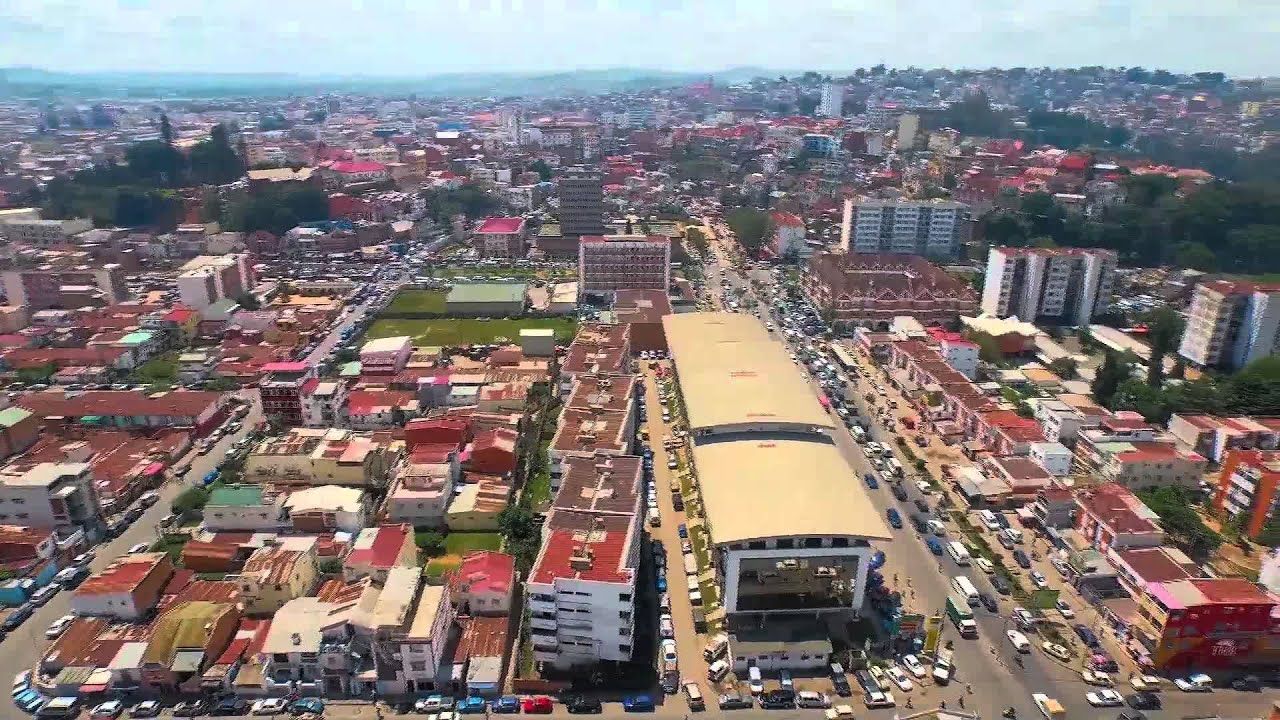 Aerial view of Antananarivo, Madagascar, with dense buildings and a central avenue with traffic and a large building.