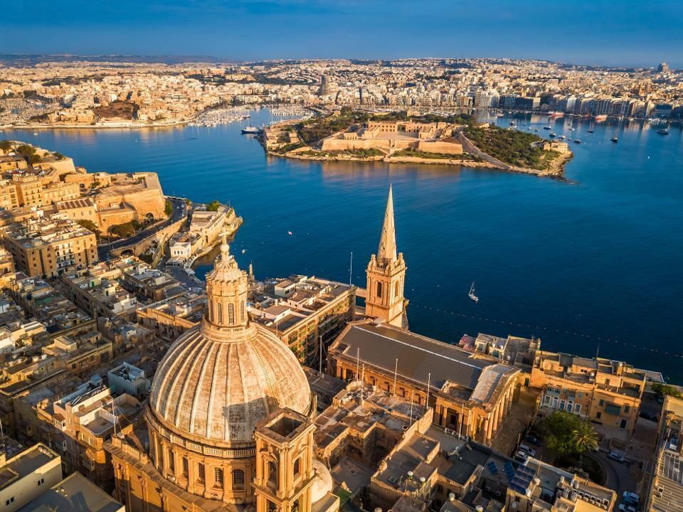 Aerial view of Valletta, Malta, with the dome of a church in the foreground, overlooking the harbor and city buildings.