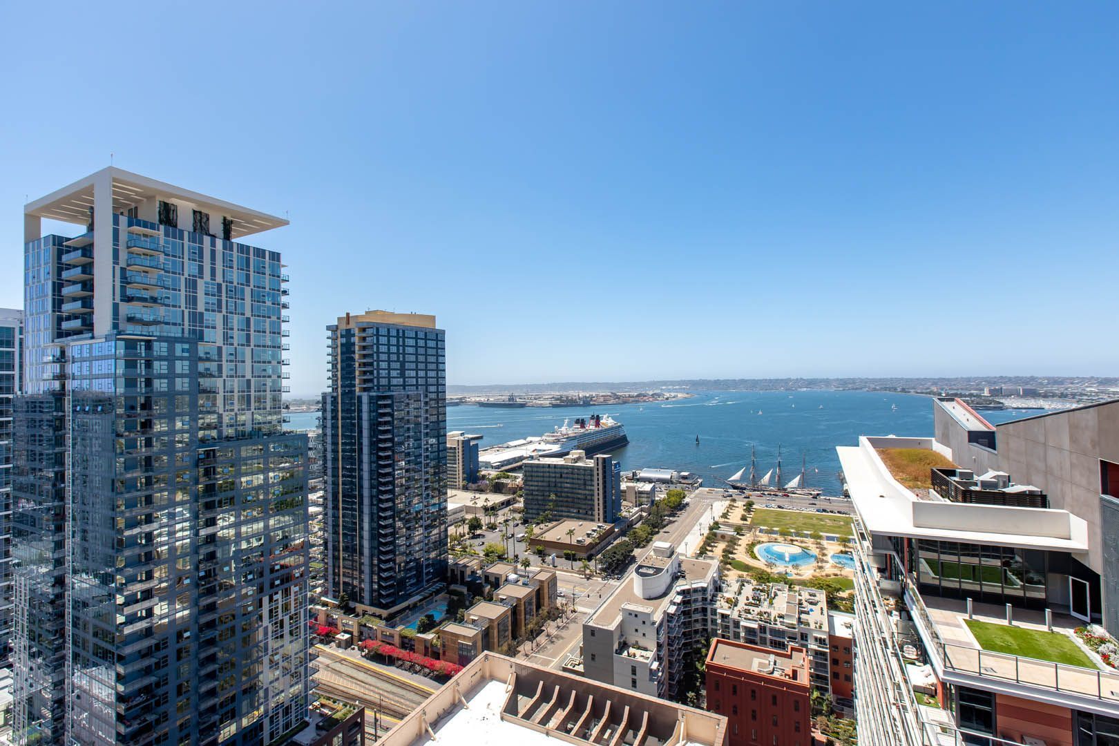 High-angle view of a city skyline overlooking a bay on a sunny day. Modern high-rise buildings stand prominently against the blue sky.